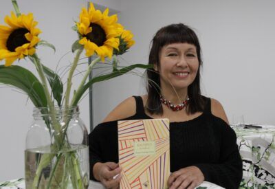 Mujer sonríe con un libro y flores